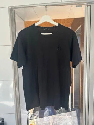 Mörkblå  t-shirt från Acne Studios - Säljer en mörkblå t-shirt från Acne Studios med klassisk passform och diskret logga  på bröstet. T-shirten har rund halsringning och är tillverkad i mjuk bomull, perfekt för en clean och stilren look. Storlek M i toppenskick