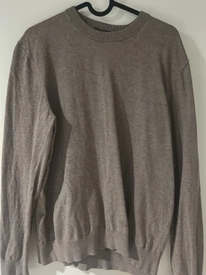 Beige slim fit tröja från H&M - En stilren beige tröja från H&M i slim fit-modell. Tröjan har rund halsringning, långa ärmar och ribbade muddar vid hals, ärmslut och nederkant. Perfekt för lager på lager och enkel att matcha med olika outfits.