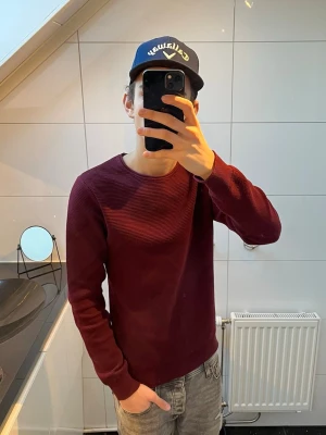 Vinröd ribbad tröja - Vinröd tröja med ribbad struktur och rund hals. Tröjan har långa ärmar och en enkel, stilren design som passar perfekt till jeans. Materialet ser mjukt och bekvämt ut. Hör av er vid minsta funderingar!