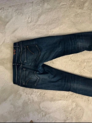 Mörkblå slim fit jeans från dondup - Säljer ett par mörkblå slim fit jeans från dondup med snygga slitningar och tvättade detaljer. Klassisk femficksmodell med orange sömmar och låg midja. Perfekta för dig som gillar en modern och avslappnad stil.
