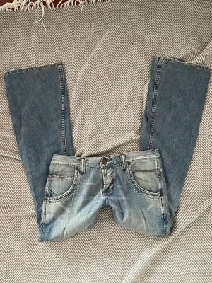 Blå bootcut jeans från Wrangler - Säljer ett par blå bootcut jeans från Wrangler med ljus tvätt och klassiska sömmar. Jeansen har fem fickor, bälteshällor och broderade bakfickor med W-detalj. Perfekt för dig som gillar retro och avslappnad stil.