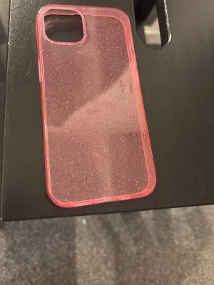 Glittrigt rosa mobilskal - Säljer ett genomskinligt rosa mobilskal med glittereffekt. Skalets kanter är rosa och hela skalet har ett snyggt skimrande utseende. Tillverkat i flexibel plast som skyddar mobilen mot repor och stötar. Passar perfekt för dig som vill ha ett skal som sticker ut. Den är tillför iPhone 15