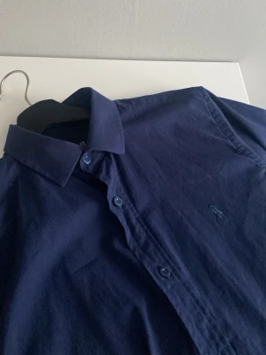 Mörkblå skjorta från Polo Ralph Lauren - Klassisk mörkblå skjorta från Polo Ralph Lauren med broderad logga på bröstet. Skjortan har lång ärm, knappar framtill och är tillverkad i mjuk bomull. Perfekt till jeans eller chinos för en clean look.