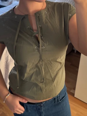 Olivgrön snörad topp från Smodell - Olivgrön croppad topp från Smodell med snörning framtill och korta ärmar. 