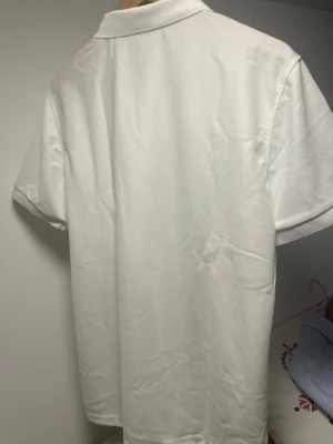 Vit pikétröja från Polo Ralph Lauren - Klassisk vit pikétröja från Polo Ralph Lauren med korta ärmar och krage. 