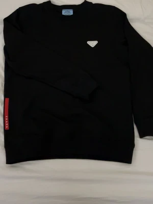 Prada tröja - Svart tröja från prada helt oanvänd och ny perfekt för dig som vill ha en lyxig och fräsch outfit, prada påse kommer också på köpet. Storleken är S men skulle säga det lutar mer mot M så det passar båda.