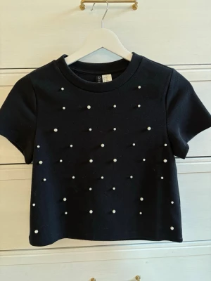 Svart stickad med pärlor - Säljer en svart stickad tröja som är kortärmad. Tröjan har massa pärlor på. Rensar garderoben. Köp helst med PostNord. Inte stickig alls. Aldrig använd