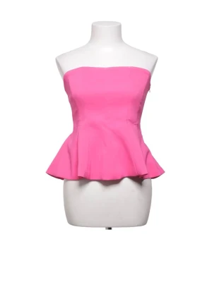 Zara Axelbandslös rosa peplum topp - Snygg axelbandslös topp i stark rosa färg från Zara med peplumskärning som ger en markerad midja och volang nedtill. Perfekt för dig som vill sticka ut! Toppens material känns som bomull eller polyester och den har en bandeauformad överdel.
