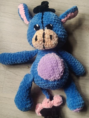 Ior mjukisdjur Nalle Puh - Säljer ett gulligt mjukisdjur i form av en åsna (Ior) virkad i blått, lila, rosa och beige plyschmaterial. Den har svarta och vita broderade ögon, rosa insida på öronen och en lila mage. Svansen har rosa och svart detalj. Perfekt som present eller dekoration. Längd 35cm