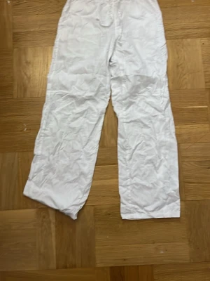 Vita vida linnebyxor med dragsko - Säljer ett par vita linnebyxor med avslappnad passform och dragsko i midjan. Byxorna har raka, vida ben. 