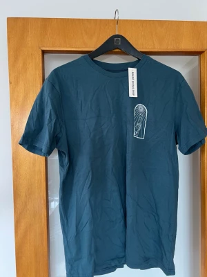 Blå t-shirt med grafiskt tryck - Snygg blå t-shirt från Malmö Locals Shop med unikt grafiskt tryck på bröstet och ryggen. T-shirten har rund hals och korta ärmar, tillverkad i mjuk bomull. Perfekt för dig som gillar streetwear och coola prints.