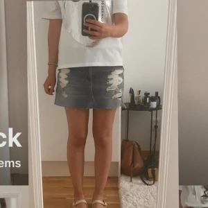 Jeanskjol med slitningar - Strl 27 men uppskattas vara liten då den är menat att ha på sig hög midjat men om man ska ha den lågt då blir den tightare. Kontakta vid funderingar🩵🩵