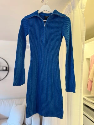 Blå ribbad stickad klänning - Säljer en blå ribbad stickad klänning med lång ärm och half zip framtill. Klänningen har en kroppsnära passform och är perfekt för dig som gillar en enkel men snygg look. Materialet är mjukt och stretchigt, vilket gör den bekväm att bära.