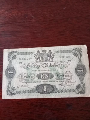 Svensk 1 krona sedel 1918 - Kotia  Unik gammal svensk 1 krona sedel från 1918, utgiven av Sveriges Riksbank. Sedeln har detaljerade ornament, riksvapnet och klassisk svartvit design med text i gammal stil. Perfekt för samlare av historiska mynt och sedlar.