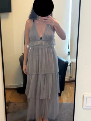 Ljusgrå långklänning med volanger glitter  - Ooootroligt fin student/ bal / sittningsklänning. Har enbart använt en gång på en sittning. Har inga fläckar eller så! Passar mig perfekt som bär storlek s. För referens är jag 168 cm och den slutar strax vid anklarna. Är en grå silver färg. Står att det är storlek M men tycker den verklgien passar normalt för mig som oftast bär s.