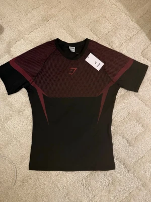 Gymshark Onyx V5 Tröja – Svart & Röd - Gymshark Onyx V5 Tröja - Svart och röd 👕 Storlek: L 🎨 Färg: Svart med röda detaljer ✨ Skick: 10/10 – i nyskick 🧵 Modell: Onyx V5