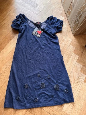 Marinblå kortklänning med puffärmar - Snygg marinblå kortklänning från Killah med puffiga kortärmar och dekorativa tygrosor nertill. Klänningen har en rund halsringning och är tillverkad i ett mjukt material som känns bekvämt mot huden. Perfekt för dig som vill ha en unik och stilren look. Skriv gärna för mått! 💕