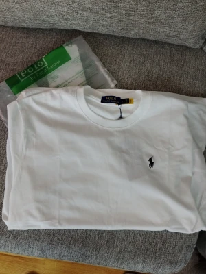 Snygg och klassisk Polo Ralph Lauren t-shirt – helt nya med etikett! - Säljer en  exklusiv, vit t-shirt från välkända märket Polo Ralph Lauren. Perfekta för dig som vill ha en tidlös och stilren bas i garderoben. Tillverkade i mjuk och skön bomull som ger hög komfort hela dagen.  Färg: Vit Storlek: XL(men sitter perfekt för oss som har L) Material: 100% bomull Kortärmad, rund halsringning Klassisk broderad Polo-logga på bröstet Helt nya med originaletiketter kvar! Skicka gärna ett meddelande vid intresse eller frågor 