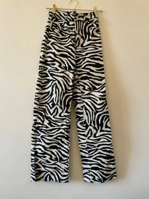 Zebramönstrade vida jeans - Säljer ett par  zebramönstrade jeans med hög midja och raka, vida ben. Svartvitt mönster som verkligen sticker ut och ger en cool statement-look. Perfekta för dig som vill ha något unikt i garderoben!