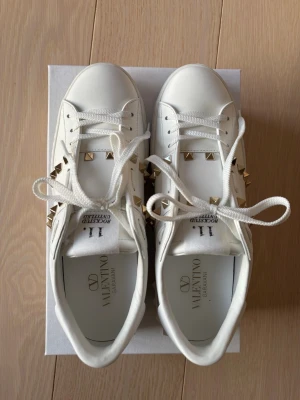 Interessekoll! Vita Valentino sneakers  - Snygga vita sneakers från Valentino Garavani med guldfärgade nitar längs sidorna. Skorna köptes nya och har endast använts en gång, därav ser de helt oanvända ut! Hör av dig vid interesse eller frågor!🩷