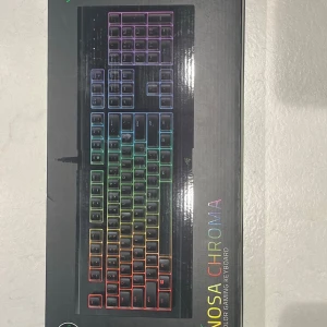 Razer Cynosa Chroma - Helt nytt - Säljer ett Razer Cynosa Chroma gamingtangentbord med RGB-belysning. Tangentbordet har svart bas och regnbågsfärgade bakgrundsbelysta tangenter. Perfekt för gaming och datoranvändning.