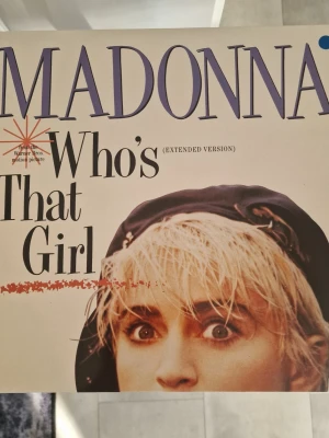 Madonna Who's That Girl singel - Singel med Madonna, 'Who's That Girl' (Extended Version), med omslag i vitt och lila text. Baksidan listar låtar och credits. Perfekt för samlare av musikrelaterade böcker och memorabilia. Inga repor.