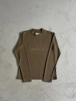 Corteiz | Waffle longsleeve knit  - Olivgrön ribbad långärmad tröja med rund hals och diskret tryck av en färja på bröstet. Tröjan har en avslappnad passform och är tillverkad i ett mjukt, stretchigt material som passar perfekt till lager-på-lager. Snygg detalj med ton-i-ton mönster framtill. Hör av er vid minsta fundering! 