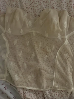 Korsett vintage  - Säljer en superfin vit korsettopp i mesh med broderade detaljer. Toppen har genomskinligt tyg med broderade mönster och hakknäppning bak. Perfekt för att styla med jeans eller kjol för en trendig look.