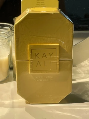 Kayali Capri In A Bottle Lemon Sugar - Kayali Capri In A Bottle Lemon Sugar är en Eau de Parfum med fräsch citrusdoft. Flaskan är elegant, åttakantig och gul med guldiga detaljer och genomskinlig kork. Doften har inslag av citron, vanilj och socker, vilket ger en söt och fräsch känsla.