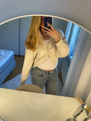 Beige twistad kofta från Gina Tricot - Trendig beige kofta från Gina Tricot med twistad detalj framtill. Koftan har en avslappnad passform, ribbade kanter och är tillverkad i mjukt stickat material. Perfekt att slänga över en topp för en chill look. Köptes för 300kr 