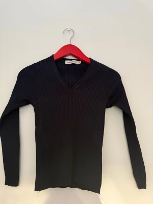 Svart ribbad v-ringad tröja Gina Tricot - Snygg svart ribbad tröja från Gina Tricot med v-ringning och lång ärm. Tröjan har en figurnära passform och är tillverkad i ett stretchigt material som sitter skönt på kroppen. Perfekt att styla med jeans eller kjol.