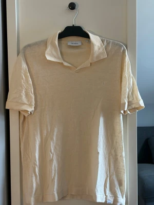 Beige linnen-polo från Les Deux - Stilren beige polo från Les Deux i luftig linne-bommuls blandning. Polon har korta ärmar, klassisk krage och en enkel, clean look utan mönster. Perfekt för dig som gillar minimalistisk stil och vill ha något svalt till sommaren.