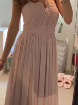 Balklänning  - Elegant ljusrosa långklänning med plisserad kjol och vackert draperad överdel. Klänningen har ärmlös design och markerad midja, vilket ger en romantisk och flowy siluett. Perfekt för speciella tillfällen och bal. Jag är 163cm och den var lite för lång men perfekt med klackar! Köpt på Vinted men är i mycket bra skick! 