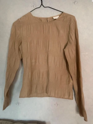 Beige blus med lång ärm från VILA - Söt beige blus med plisserad struktur och rund halsringning. Tillverkad i ett lätt, något transparent material som ger en luftig känsla. Långa ärmar och rak passform gör den enkel att styla till olika looks. Säljer då jag inte använt plagget, kan skicka bild på om det skulle begäras❤️