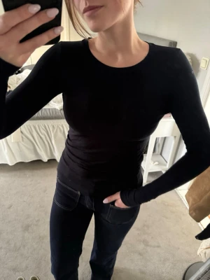 Mörkblå långärmad topp i bomull - En stilren mörkblå långärmad topp med rund halsringning. Toppen är figurnära och tillverkad i mjuk bomull, perfekt att matcha med jeans eller kjol. Enkel och tidlös design som passar till många olika looks.