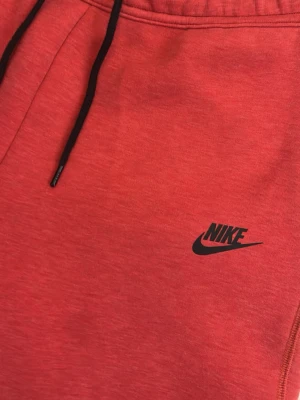 Röda mjukisbyxor från Nike - Snygga röda Nike tech byxor. Svarta snören som man lätt kan snöra för en snyggare passning. Perfekta för både träning och häng.