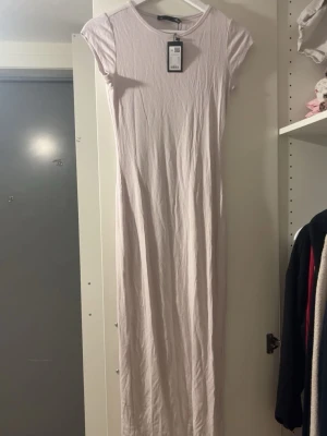 Ljusbeige  långklänning  - En stilren och enkel långklänning i ljusbeige. Klänningen har rund halsringning och korta ärmar. Tillverkad i mjukt bomullsmaterial som ger en bekväm känsla. Perfekt för en avslappnad och trendig look.