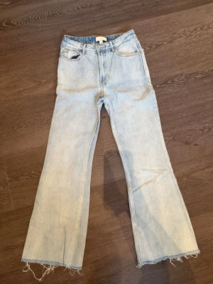 Ljusblå utsvängda jeans med stjärndetaljer - Säljer ett par ljusblå jeans med utsvängda ben och råa, fransiga benslut. Baksidan har coola stjärnformade detaljer på fickorna som ger en unik look. Perfekta för dig som vill sticka ut med din stil. Klassisk femficksmodell i denim.
