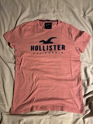 Rosa Hollister t-shirt med tryck - Tjena! Säljer nu denna rosa hollister tishan då jag ej vill ha den (inte ens provat den). Trycket på bröstet är mörkblått och den är i storlek S.