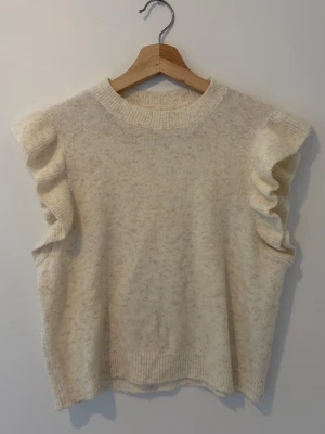 Beige ärmlös stickad tröja med volang - Superfin beige stickad tröja utan ärmar och med volangdetaljer vid axlarna. 