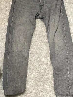 Grå jeans med rak passform - Säljer ett par grå jeans med rak passform och klassisk femficksdesign. Jeansen har en snygg tvättad look och är tillverkade i denim. Perfekta för dig som gillar en avslappnad och tidlös stil. Mdd en storlek med 31 32