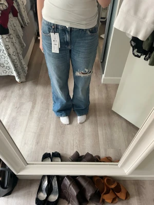 Blå baggy jeans Gina - Säljer ett par blå baggy jeans från Gina tricot med slitningar och hål på ena låret. Jeansen har baggy passform, klassisk femficksmodell och medelhög midja. Perfekta för en avslappnad och trendig look. Nypris 499!