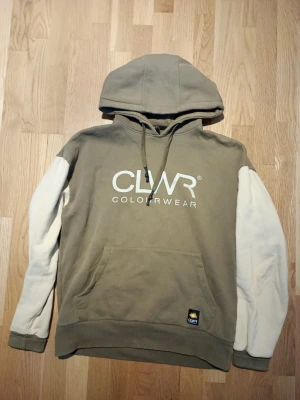 CLWR hoodie med kontrastärmar - Snygg hoodie från CLWR ColourWear i olivgrönt med vita kontrastärmar. Stor huva med dragsko, magficka och tryckt logga på bröstet. Mjuk bomullsmix och ribbade muddar. Perfekt för en avslappnad streetstyle-look.