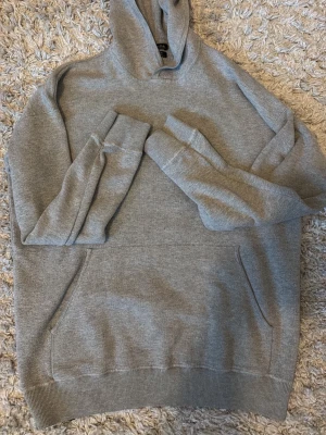Grå hoodie från Massimo Dutti - Snygg grå hoodie från Massimo Dutti i mjuk bomull. Klassisk modell med huva och känguruficka framtill. Perfekt för en avslappnad stil och enkel att matcha med jeans eller joggers.