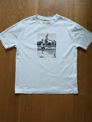 Vit t-shirt med baskettryck - Vit t-shirt med ett svartvitt tryck av en basketspelare på bröstet. Strl S. Väldigt bra skick. Riktigt skönt material. Säljer för den börjar bli för liten. 