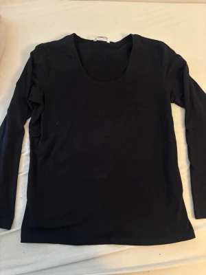 Svart långärmad topp från JoyLove - En enkel och stilren svart långärmad topp från JoyLove. Toppen har rund halsringning och är tillverkad i ett mjukt material som känns skönt mot huden. Perfekt att matcha med jeans eller kjol för en clean look.