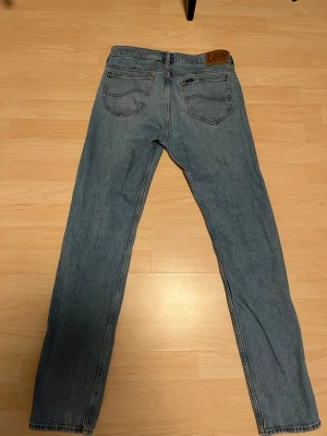 Blå raka jeans från Lee - Klassiska blå jeans från Lee med rak passform och fem fickor. Jeansen har en ljus tvätt och Lee-lapp bak i midjan. Tillverkade i slitstarkt denimtyg, perfekta för en avslappnad och tidlös stil.