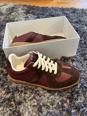 Bruna och vinröda sneakers i mocka - Snygga sneakers i brunt och vinrött med ovandel i mocka och läder. Skorna har vita snören, beige innersula och en klassisk gummisula. Perfekt för dig som gillar retrostil och vill sticka ut med en unik färgkombo.