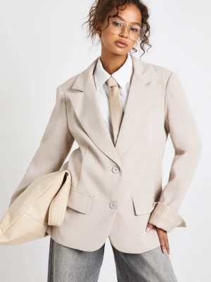 Beige oversized kavaj - Stilren beige oversized kavaj med breda slag och två knappar framtill. Kavajen har fickor med lock och synlig rutmönstrad innermudd vid ärmslut. Perfekt för en trendig och avslappnad look. Oanvänd! Nypris är 800