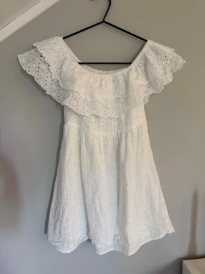 Vit klänning Meet Me There - Söt vit kortklänning från Meet Me There med offshoulder-modell och dubbla volangdetaljer upptill. Klänningen är i broderad bomull med hålmönster och har en luftig, somrig känsla. Perfekt strandklänning!🥰Säljer då den är för kort på mig som är 166cm. Den är i XXS/XS! Säljer för 230kr